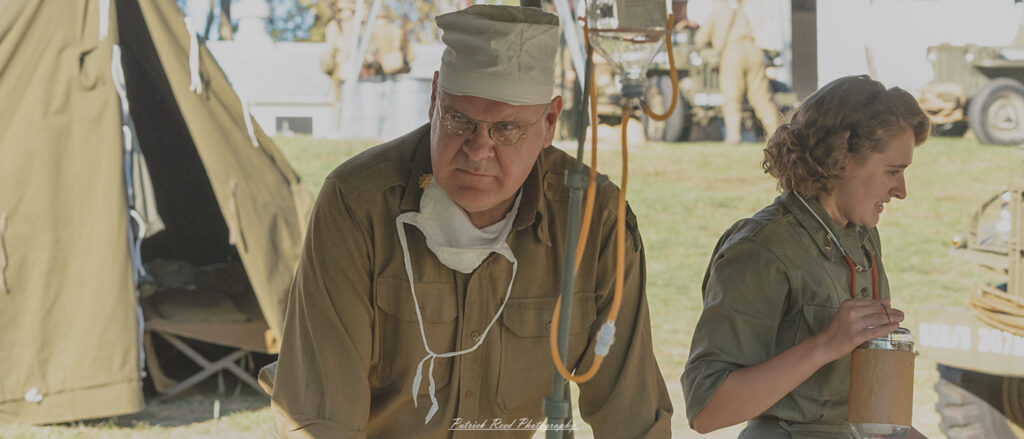 "Portrait of a U.S. Army surgeon in a WWII-era field hospital setting. The surgeon, wearing a military uniform and surgical scrubs, stands confidently with a stethoscope around his neck and a focused expression. Behind him, medical equipment and supplies are visible, along with a backdrop of canvas tents that suggest a wartime medical environment. The image captures the dedication and professionalism of military medical personnel in the face of adversity."